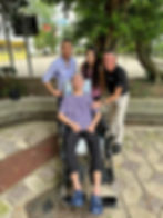 Four people, one in a wheelchair, smiling outdoors.