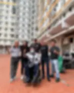 Six people, one in a wheelchair, smiling and giving thumbs up