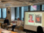 Two men presenting at an event, with headshots on a projector screen